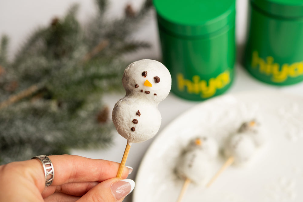 Snowman cake pops made from a chocolate-almond flour batter dipped in yogurt and decorated with dark chocolate eyes and a fruit nose.