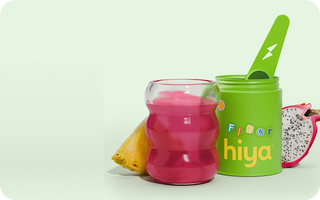 Pink kids' fiber drink in glass next to green Hiya jar with spoon, pineapple & dragon fruit slices