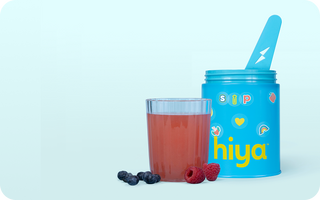 Blue kids' nutrient powder container with spoon, berry drink, and fresh raspberries & blueberries