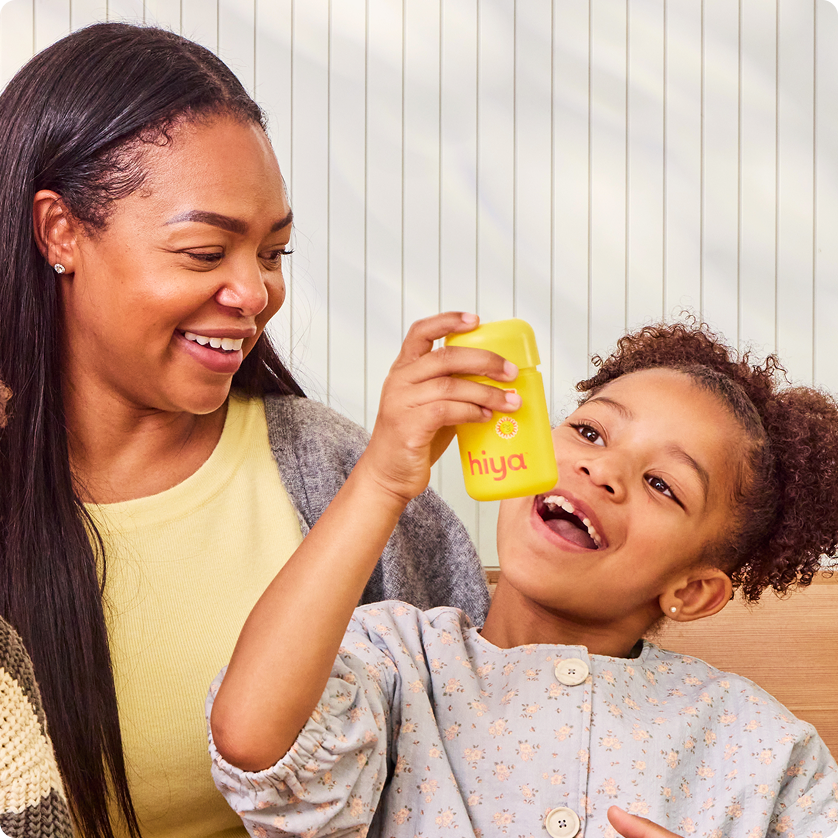 Mom and child smiling with yellow Hiya vitamin bottle, promoting kids' nutrition and healthy choices