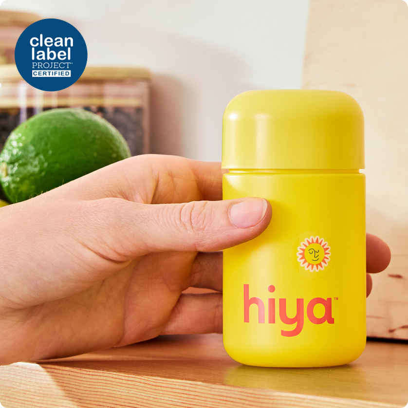 Yellow Hiya kids vitamin bottle with clean label certification, held in hand near lime