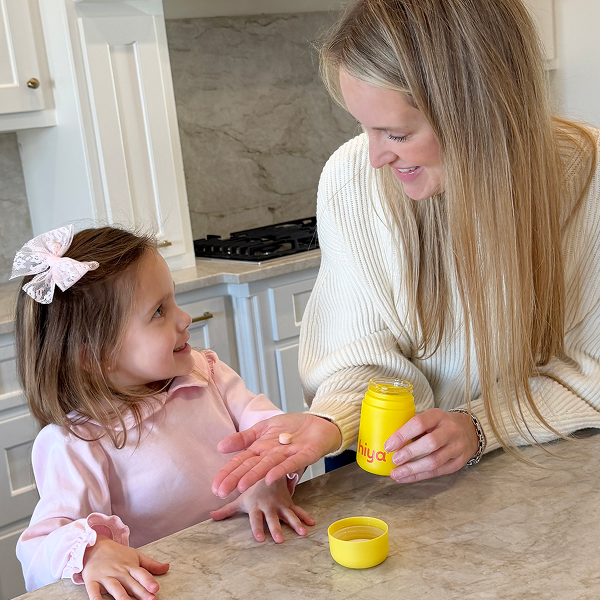 Mom giving child a vitamin tablet from yellow bottle in kitchen