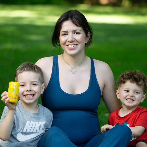 Mom and two kids smiling outdoors, child holding yellow vitamin tablet bottle
